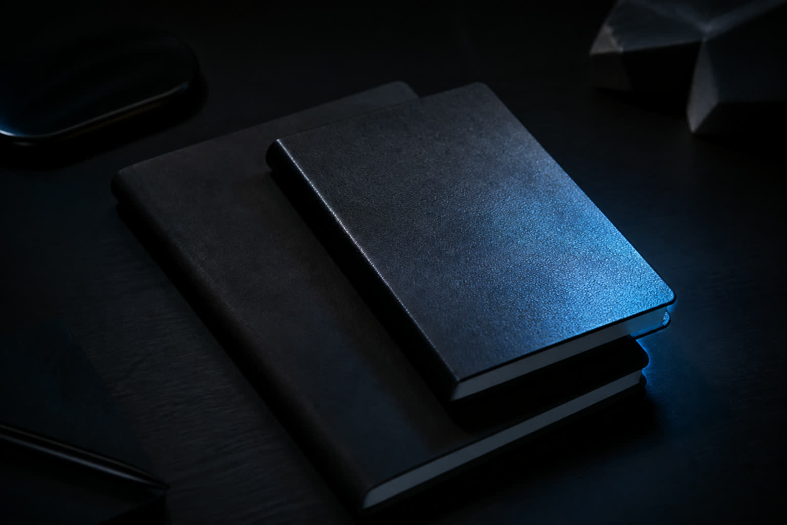 Two notebooks overlapping on a dark desk, one page catching a blue edge light